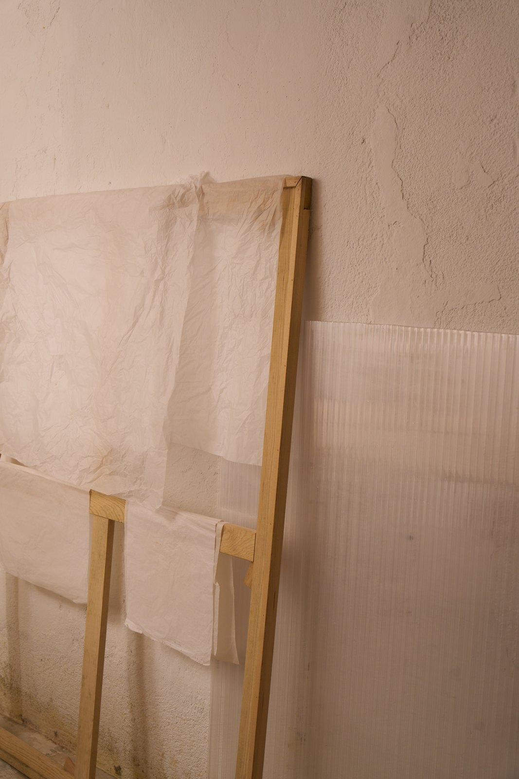 Bastidor de madera con papel apoyado contra la pared junto a placas de policarbonato