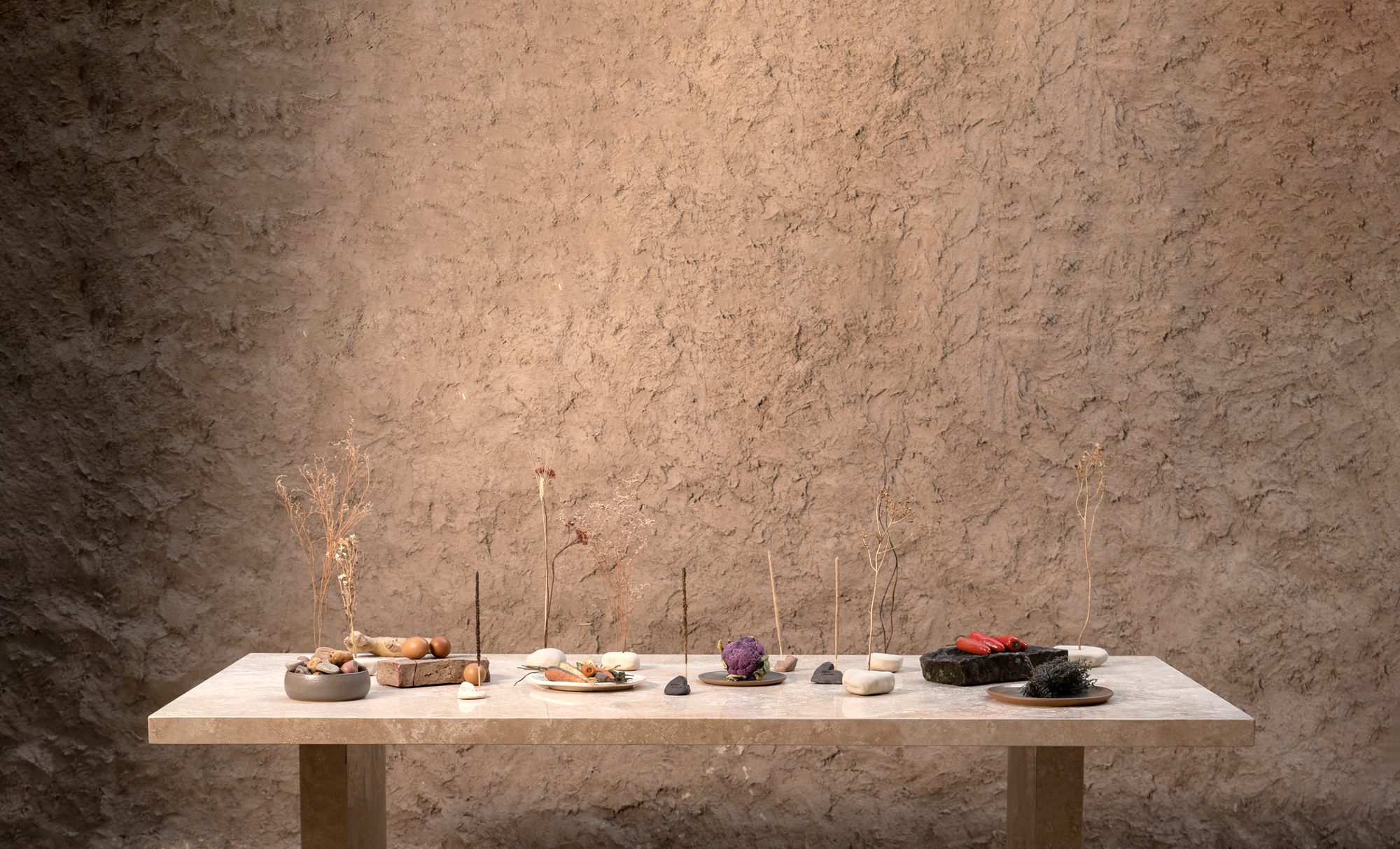 Mesa larga de travertino con piedras de cerámica, platos, ramas secas y verduras contra una pared de barro