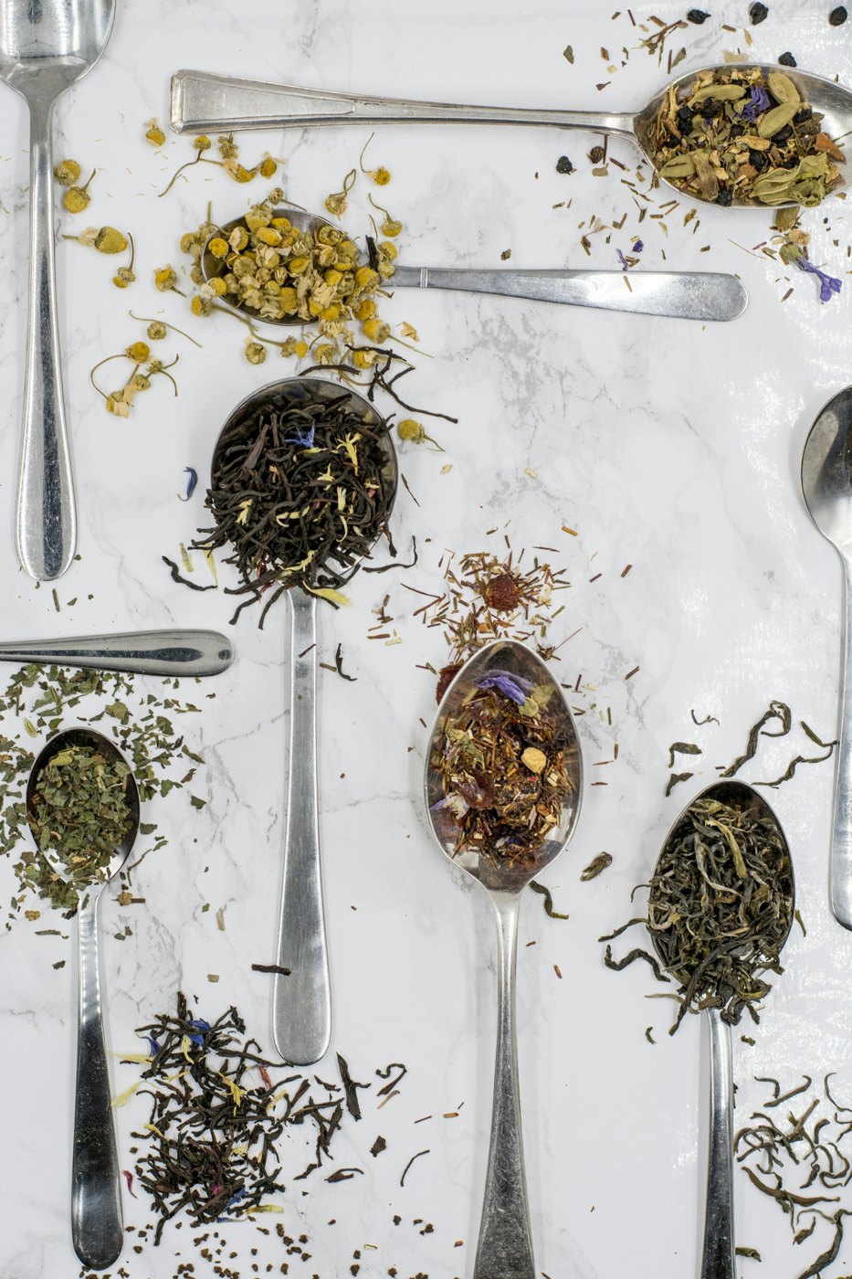 Cucharas con distintos tés y flores secas sobre mármol