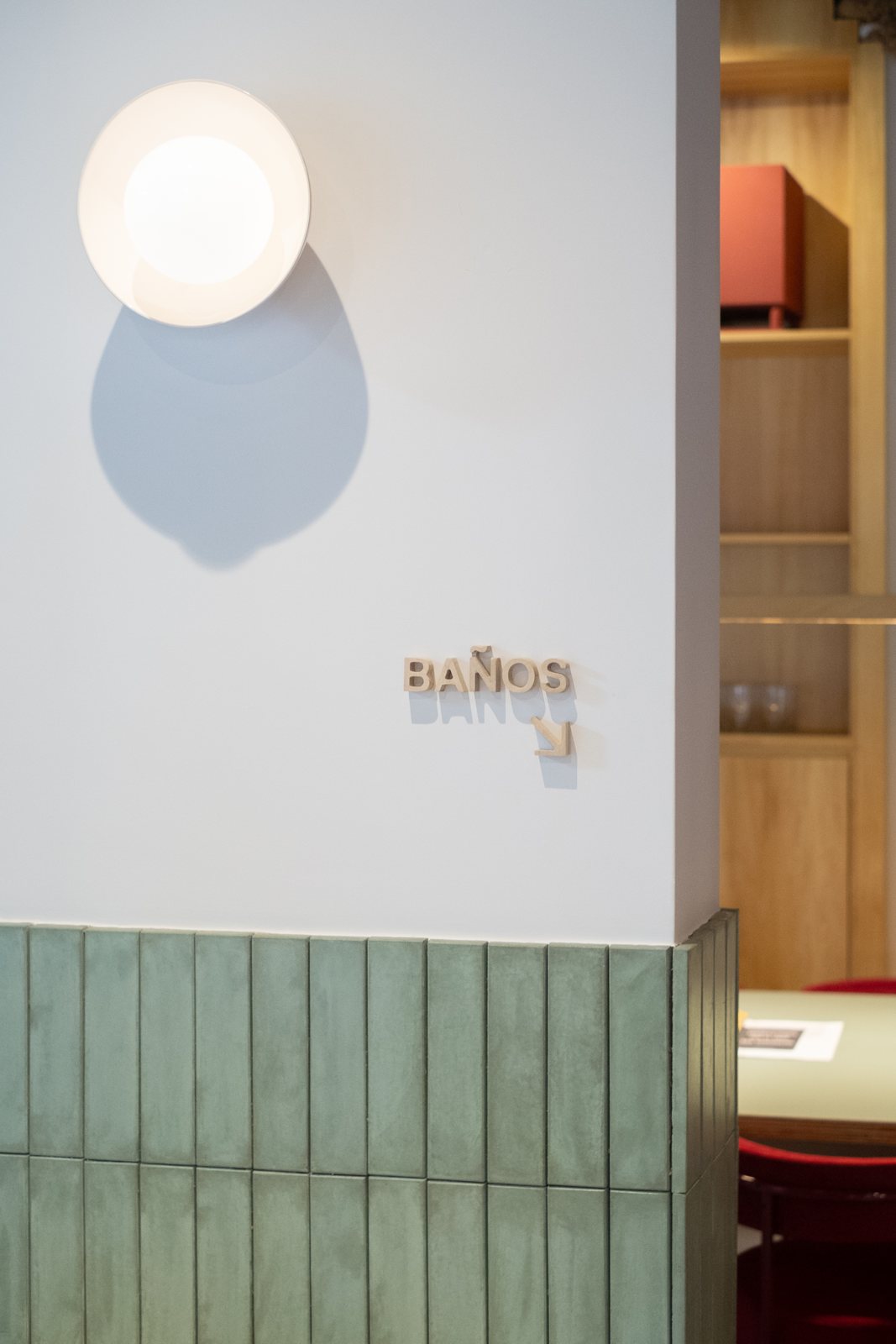 Letras de madera BAÑOS con flecha sobre pared blanca